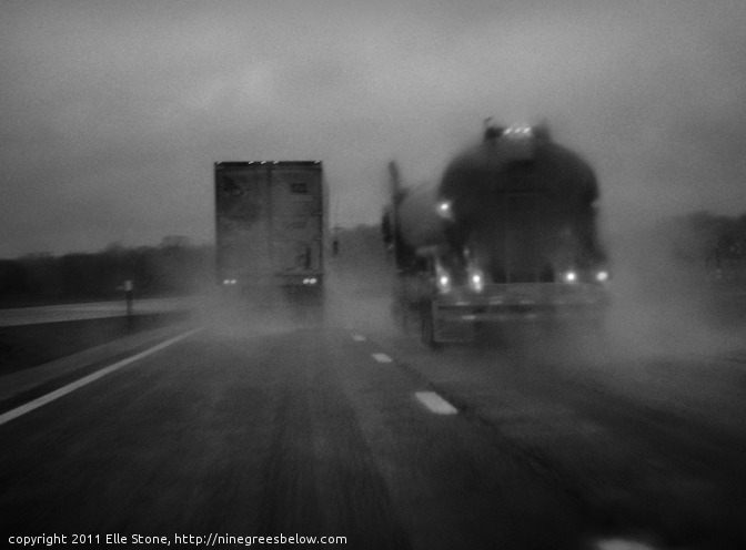 One truck passes another during a heavy rain storm, casting spray into the air.